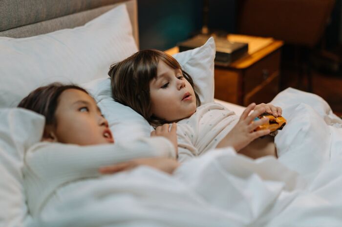 Two children lying in bed, one holding a toy car, demonstrating trust and companionship.