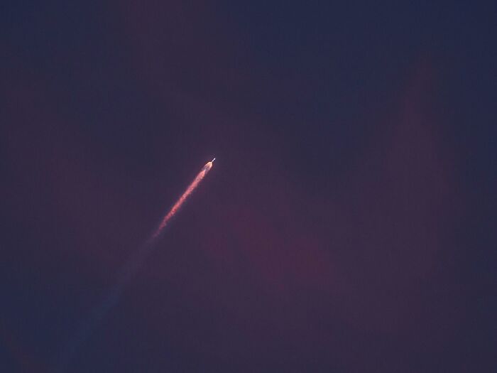 Rocket in the night sky, leaving a bright trail, surrounded by dark clouds, evoking conspiracy theories.
