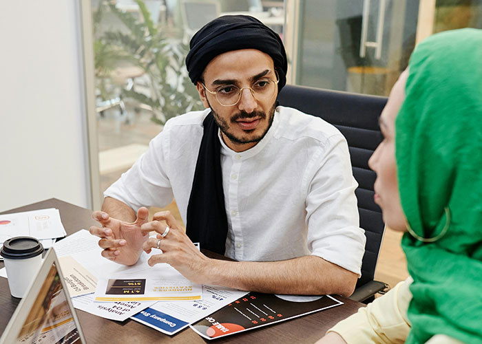 Man with glasses and head wrap discussing ideas at meeting, showing indicators of being super smart and hiding it well.