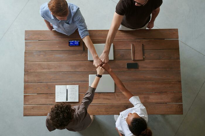 People fist-bumping over a wooden table with notebooks and phones, symbolizing unity in discussing chilling conspiracy theories.