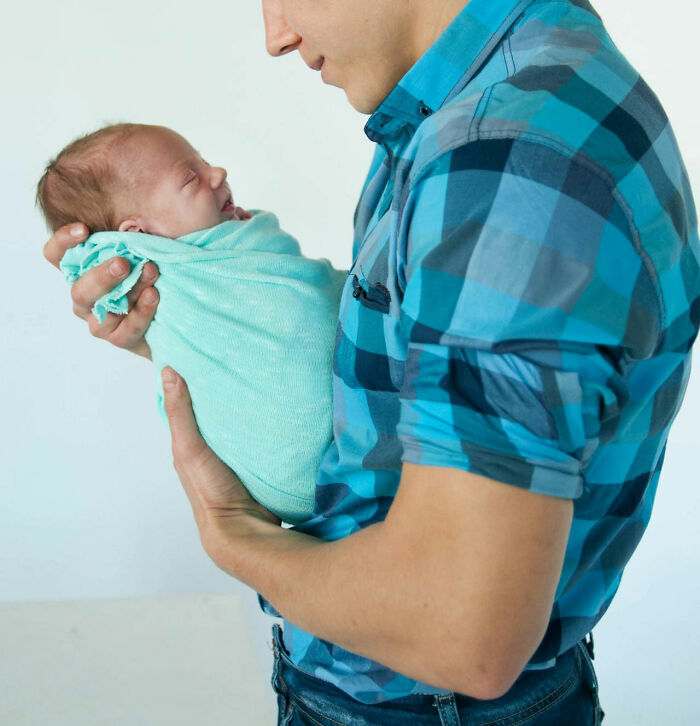 A man in a blue checkered shirt holding a baby wrapped in a teal blanket, symbolizing family-secrets.