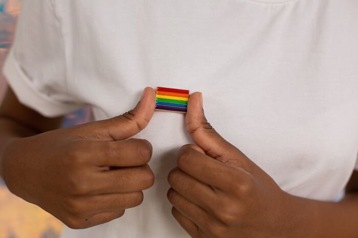 Person wearing a white shirt holding a rainbow badge, symbolizing diversity and unity despite being outnumbered.