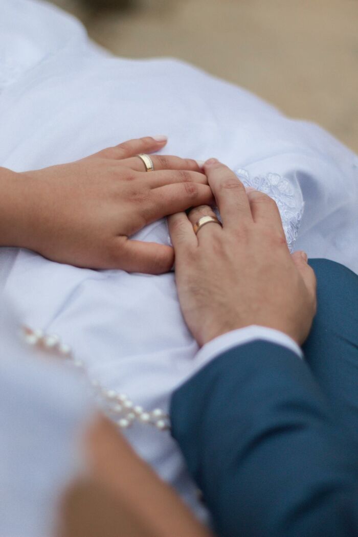 Hands with wedding rings on a white dress, symbolizing family secrets.
