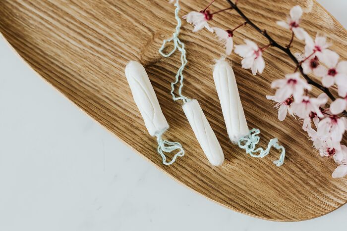 Three tampons on a wooden tray with pink flowers, illustrating the concept of questions concerning women's products.