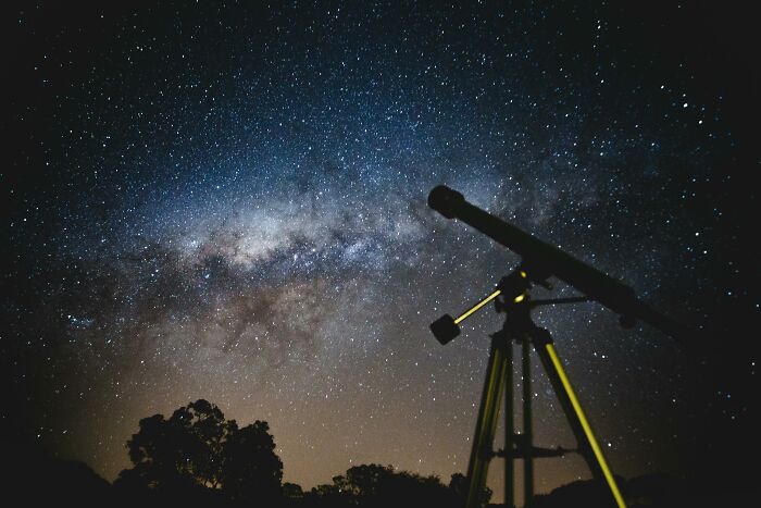 Telescope silhouetted against a starry night sky, capturing the Milky Way in a clear and expansive view.