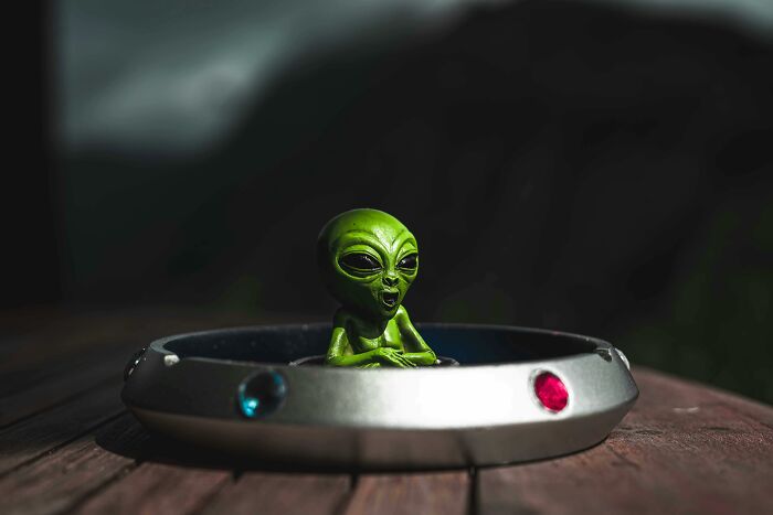 A small green alien figure inside a miniature UFO model, symbolizing conspiracy theories.