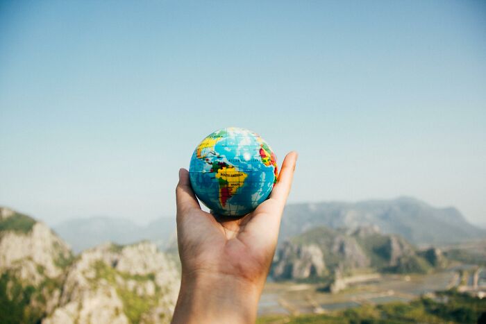 Hand holding a small globe against a scenic mountain backdrop, symbolizing conspiracy theories and global mysteries.