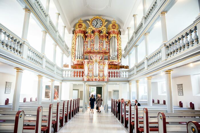 Interior of a wedding venue with a grand organ and guests seated in wooden pews.