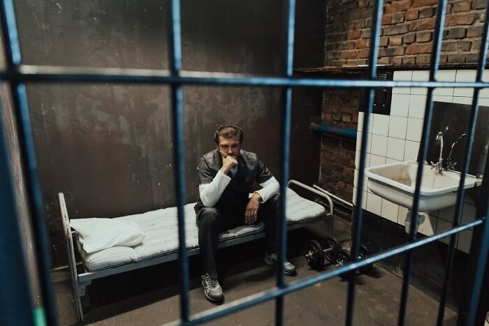 Man sitting on a bed in a dimly lit prison cell, contemplating a change in stance on vaccinations.