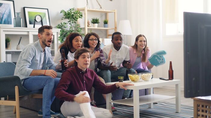 Group of friends excitedly watching TV, expecting to get their way, with snacks on the table.