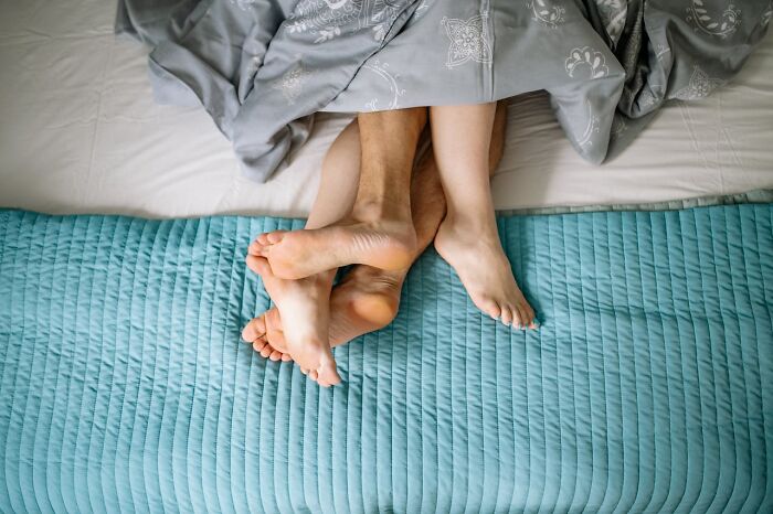 Feet entangled under a gray blanket on a bed, symbolizing hidden family secrets.