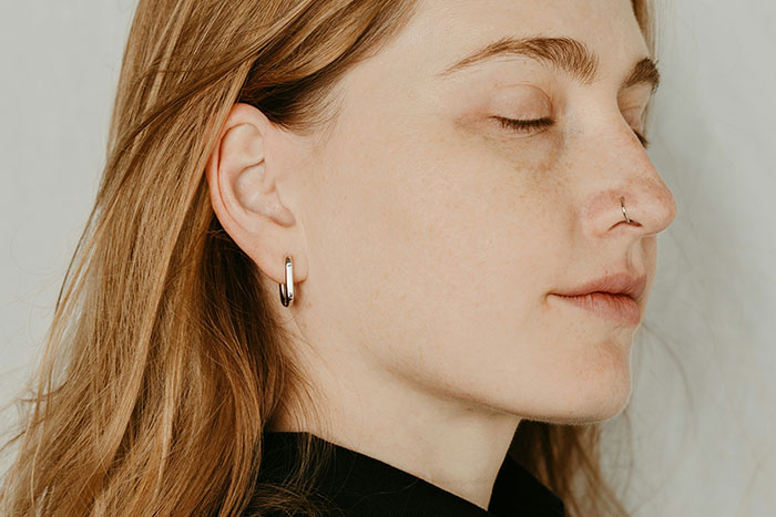 Young woman in profile view with closed eyes, wearing hoop earrings and a nose ring.