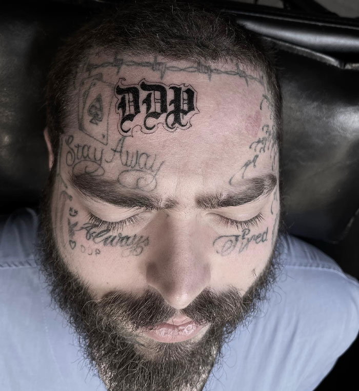 A close-up of Post Malone with his eyes closed, showcasing his facial tattoos prominently, including "Stay Away" and "DDP" on his forehead. A close-up of Post Malone with his eyes closed, showcasing his facial tattoos prominently, including "Stay Away" and "DDP" on his forehead.