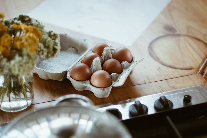 Carton of brown eggs on a wooden table next to a stove and flowers, illustrating simple kitchen questions.