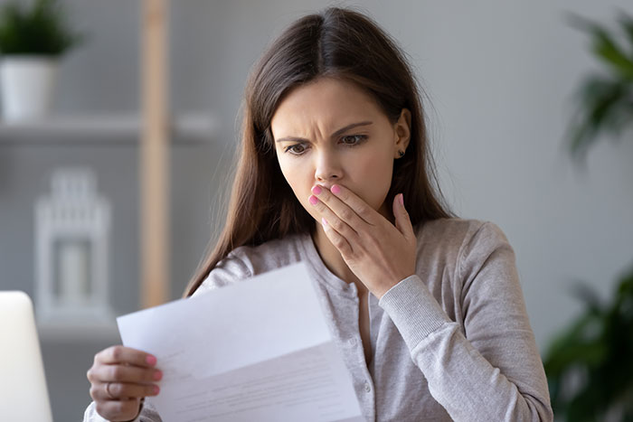 Woman looking shocked at a document, possibly related to unexpected wedding costs.