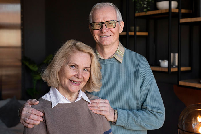 Elderly couple smiling indoors, with warm lighting and modern decor in the background.