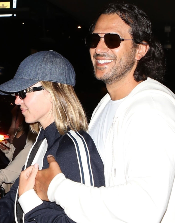Sydney Sweeney, dressed casually in a dark jacket with white stripes and a denim baseball cap, is seen walking closely with Jonathan Davino, who wears a white hoodie and sunglasses. Jonathan smiles broadly as he wraps an arm affectionately around Sydney's shoulders. The setting appears to be at night, with both dressed in relaxed attire, enjoying their time together. Sydney Sweeney, dressed casually in a dark jacket with white stripes and a denim baseball cap, is seen walking closely with Jonathan Davino, who wears a white hoodie and sunglasses. Jonathan smiles broadly as he wraps an arm affectionately around Sydney's shoulders. The setting appears to be at night, with both dressed in relaxed attire, enjoying their time together.
