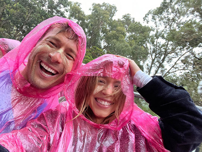 Sydney Sweeney and a friend are wearing bright pink rain ponchos, laughing together in an outdoor setting. Both have sand on their faces, suggesting they recently had a playful or windy experience at the beach. They look happy and carefree, enjoying the rainy day surrounded by trees. Sydney Sweeney and a friend are wearing bright pink rain ponchos, laughing together in an outdoor setting. Both have sand on their faces, suggesting they recently had a playful or windy experience at the beach. They look happy and carefree, enjoying the rainy day surrounded by trees.
