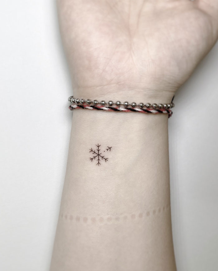 Minimalist snowflake wrist tattoo on woman’s arm with bracelets.