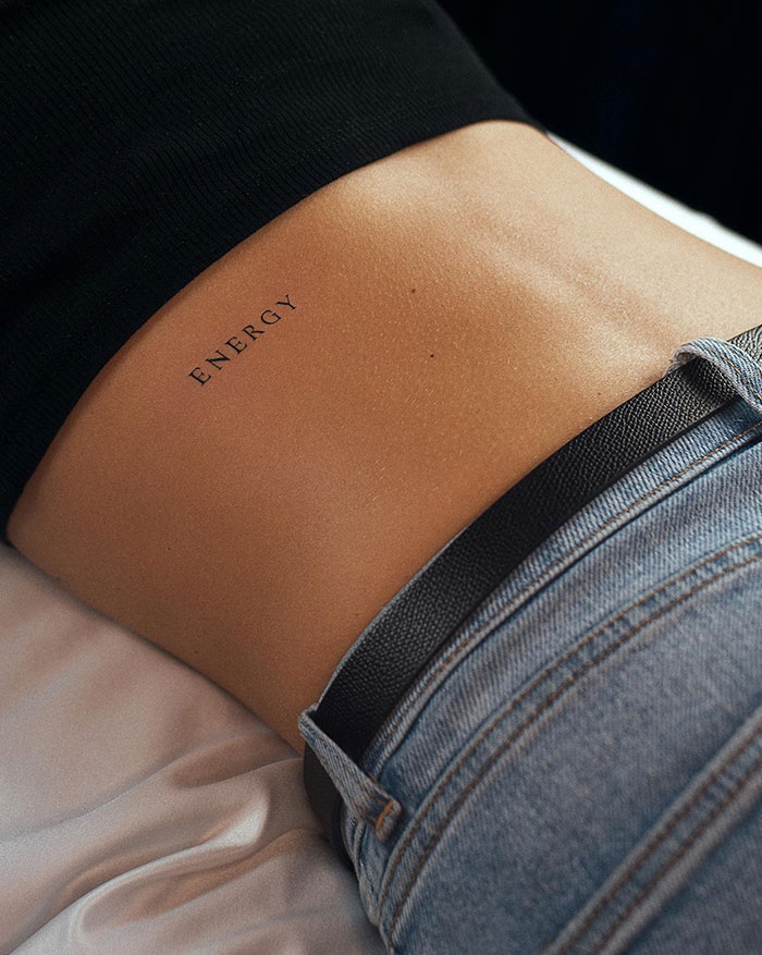 Lower back tattoo with the word "Energy" on a woman's skin, featuring subtle design.