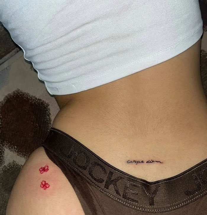 Small "carpe diem" tattoo and red flower tattoos on a woman's waist.