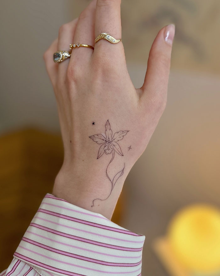 Delicate flower tattoo on woman's hand with gold rings, showcasing subtle tattoo ideas.