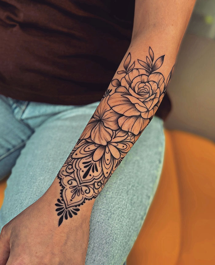 Floral tattoo design on a woman's forearm, featuring intricate patterns and bold lines.