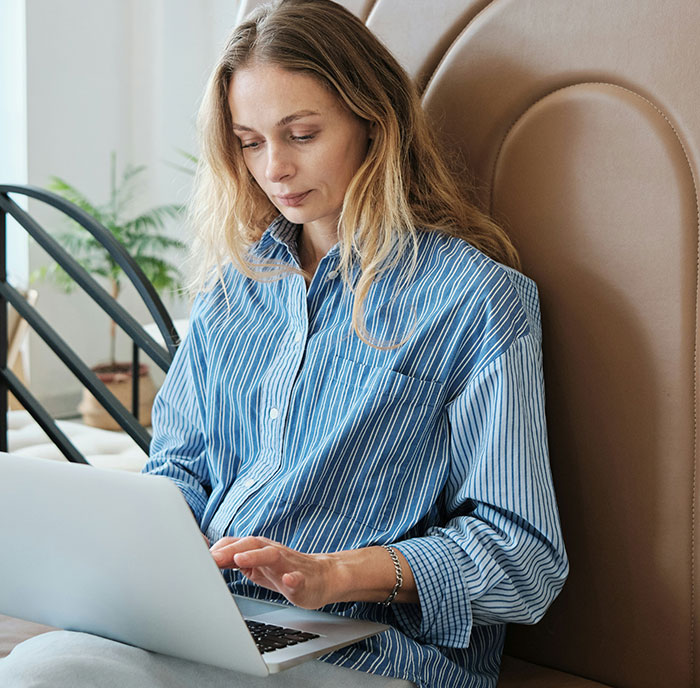 Woman in a blue striped shirt sits on a couch, using a laptop. Woman in a blue striped shirt sits on a couch, using a laptop.