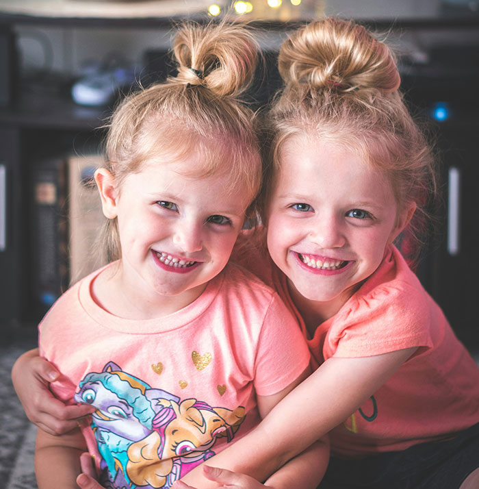 Twins smiling in matching pink shirts at home, highlighting sibling connection. Twins smiling in matching pink shirts at home, highlighting sibling connection.