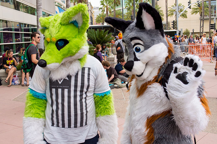 Two people in colorful animal costumes at an outdoor event, surrounded by onlookers.