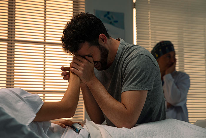Man holding hands, appearing emotional in a hospital room, related to having a baby at 15.