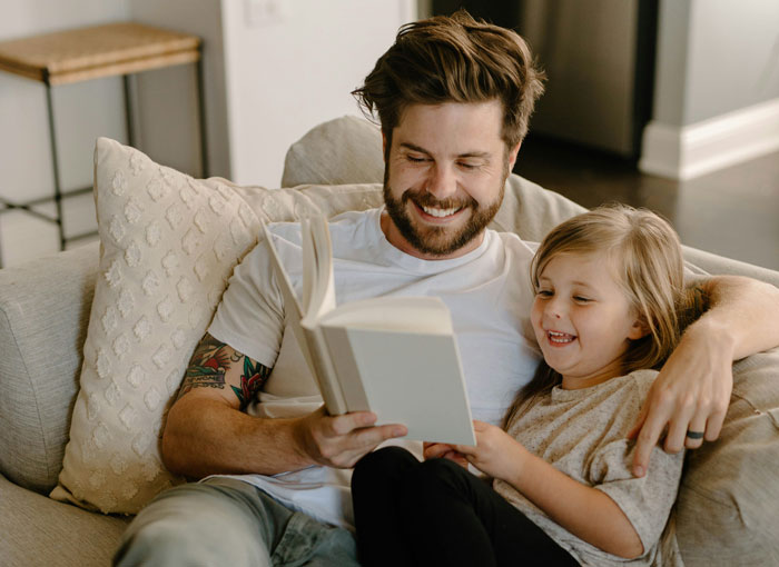 Man and child reading on couch, enjoying vacation time together. Man and child reading on couch, enjoying vacation time together.