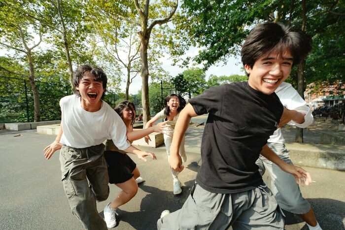 Group of smiling people running together outdoors under trees.