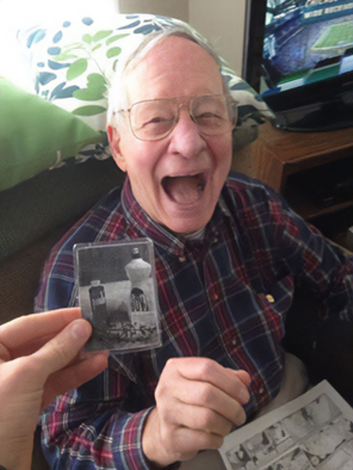 Elderly man smiling while holding a vintage black-and-white photo, embodying wholesome Thanksgiving joy.