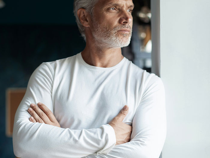 Man in a white shirt looking out a window, contemplating support for kids amidst family tension.