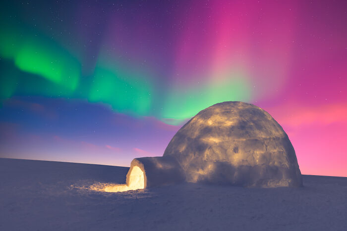 Lit igloo under vibrant aurora borealis, showcasing nature's beauty and mystery.