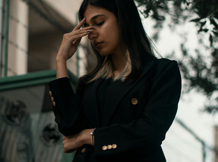 Woman in a dark pantsuit looking contemplative outdoors.