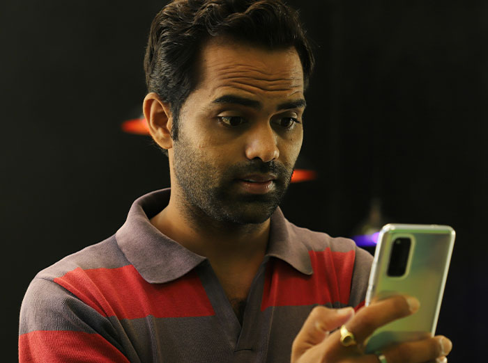 Man looking at a smartphone in surprise while indoors, expressing emotions about a wedding guest's pantsuit outfit choice.
