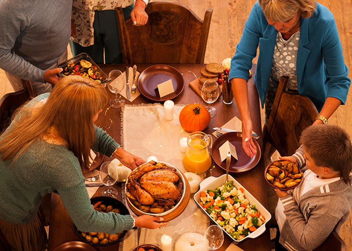 Family setting a table for Thanksgiving dinner with roast and salad, adults and child arranging dishes and table setting. Family setting a table for Thanksgiving dinner with roast and salad, adults and child arranging dishes and table setting.