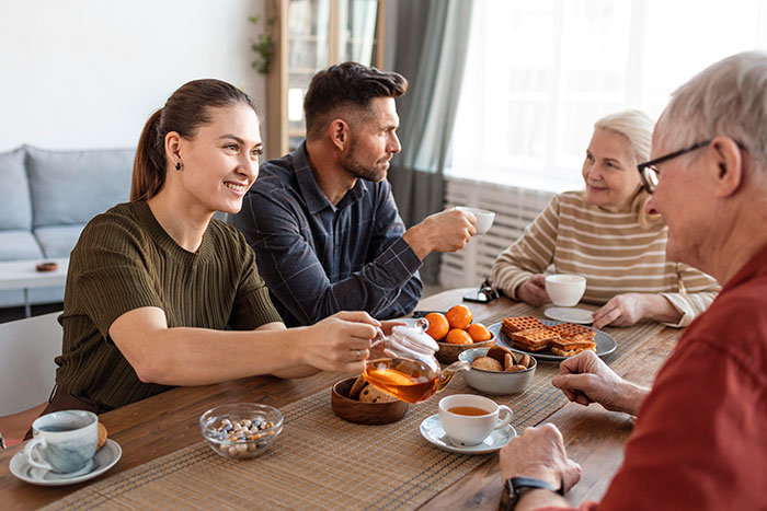 Family enjoying tea and snacks in a cozy apartment, laughing and engaging in conversation.