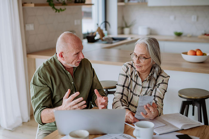 Husband and wife discussing family matters at a kitchen table, with papers and a laptop. Husband and wife discussing family matters at a kitchen table, with papers and a laptop.