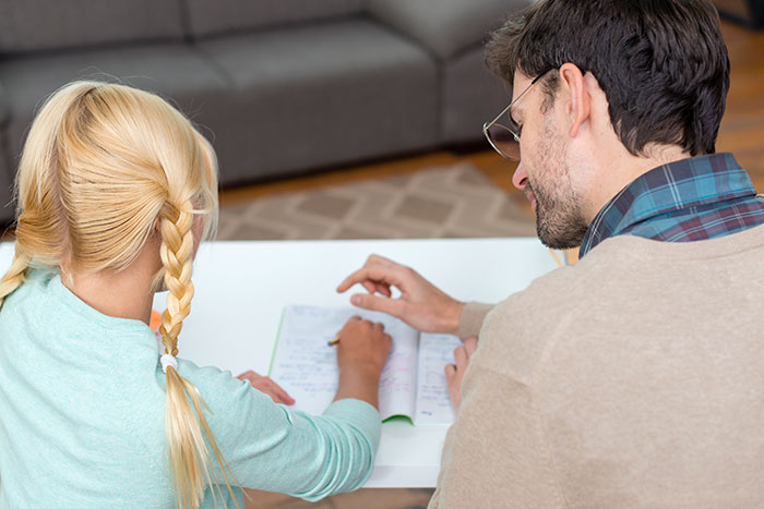 Father and daughter sitting at a table, father pointing at daughter's notebook, family relationship discussion. Father and daughter sitting at a table, father pointing at daughter's notebook, family relationship discussion.