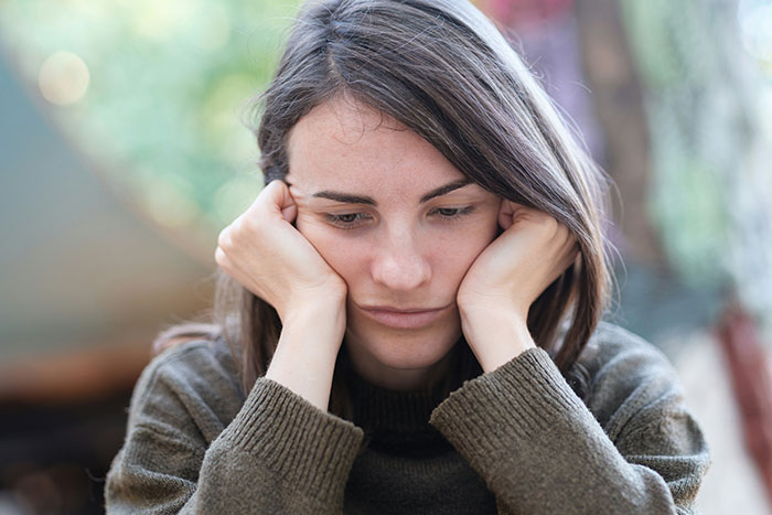 Woman looking upset and pensive, resting her chin on her hands, with blurred outdoor background. Woman looking upset and pensive, resting her chin on her hands, with blurred outdoor background.
