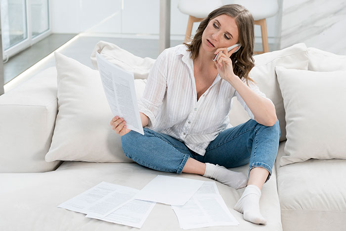 Woman in casual attire on phone, holding documents, discussing family's hypocritical husband's exclusion from will. Woman in casual attire on phone, holding documents, discussing family's hypocritical husband's exclusion from will.