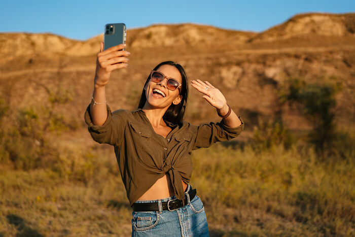 Woman taking a selfie in sunglasses and casual attire outdoors, related to daughters' exotic trip.