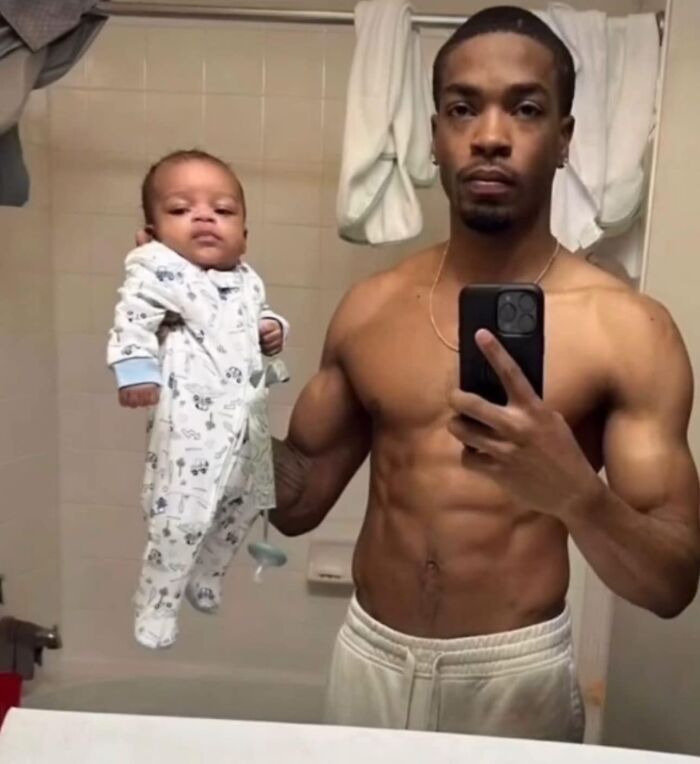 Shirtless man holds a baby while taking a mirror selfie, resembling an eclectic album cover image.