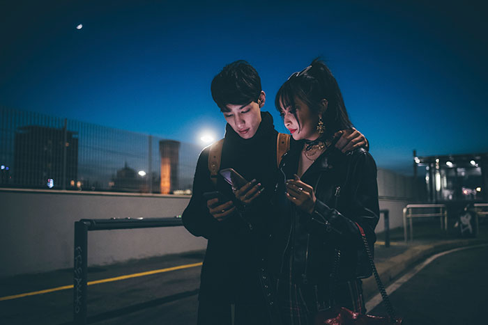 Couple standing close at night, looking at a phone; woman reflects on her boyfriend's actions. Couple standing close at night, looking at a phone; woman reflects on her boyfriend's actions.