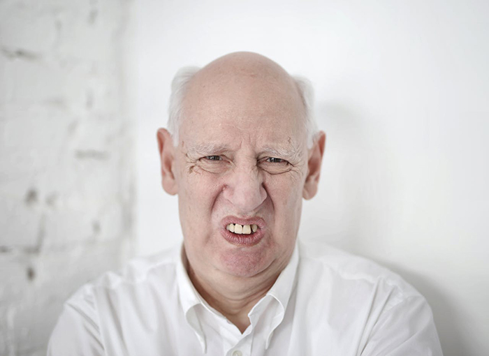 Elderly man with a displeased expression wearing a white shirt against a white background.