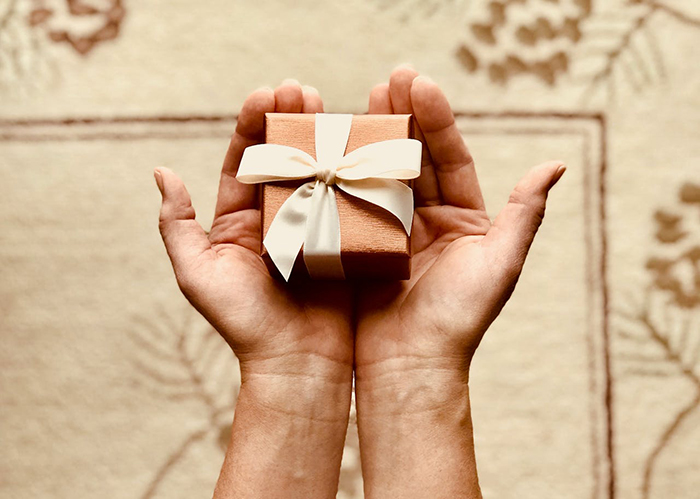 Hands holding a gift box with a white ribbon, symbolizing a baby shower gift. Hands holding a gift box with a white ribbon, symbolizing a baby shower gift.