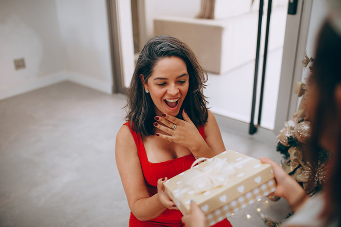 Woman in a red dress receiving a gift, looking surprised and delighted.
